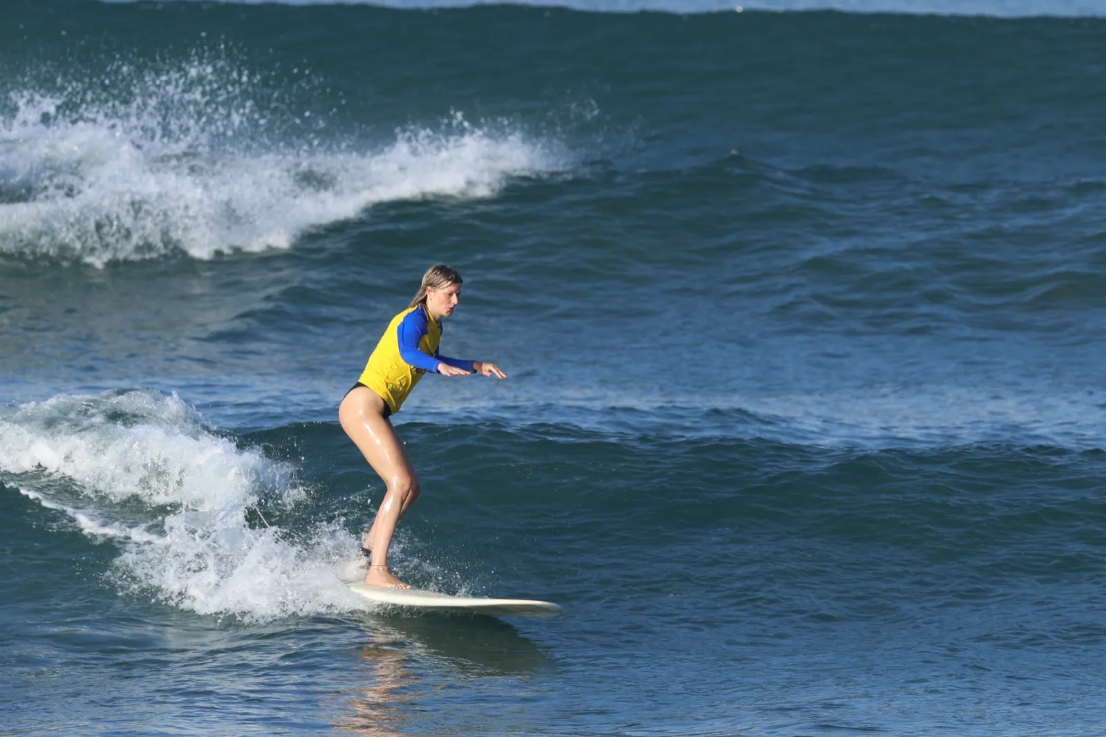 A surfer riding the white water straight toward the beach on a bright Canggu morning
