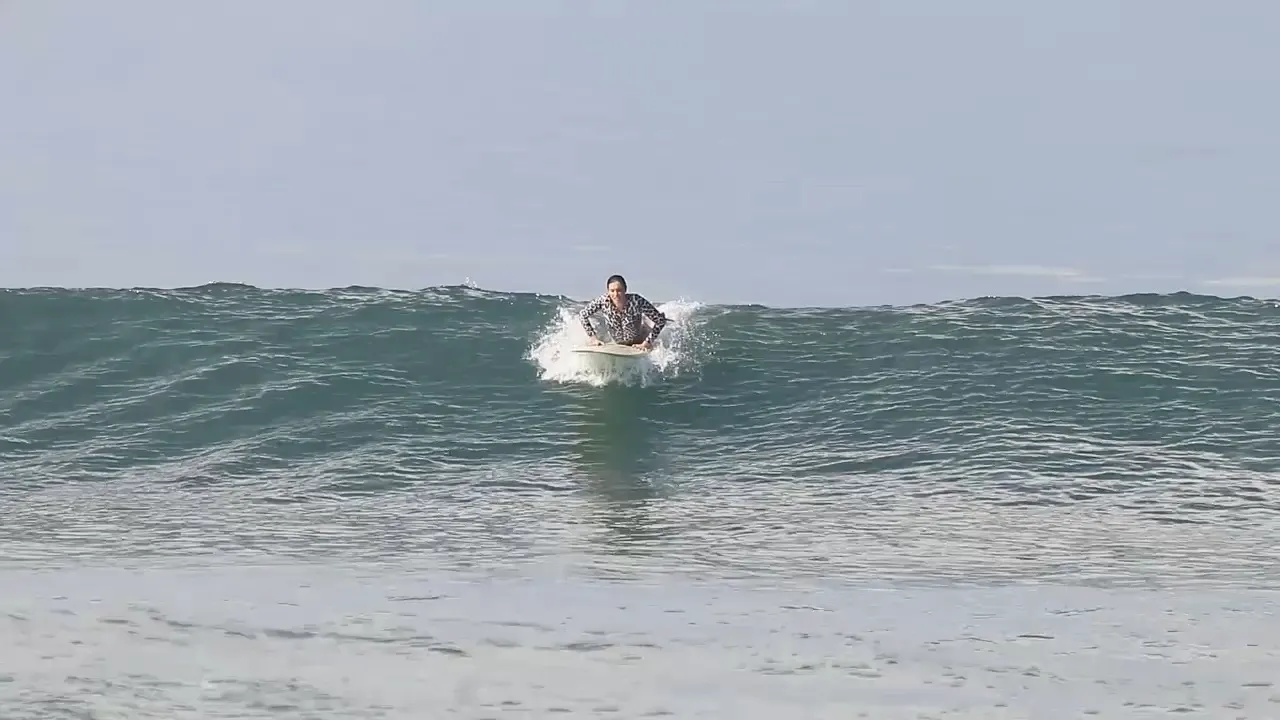 A surfer riding the white water straight toward the beach on a bright Canggu morning